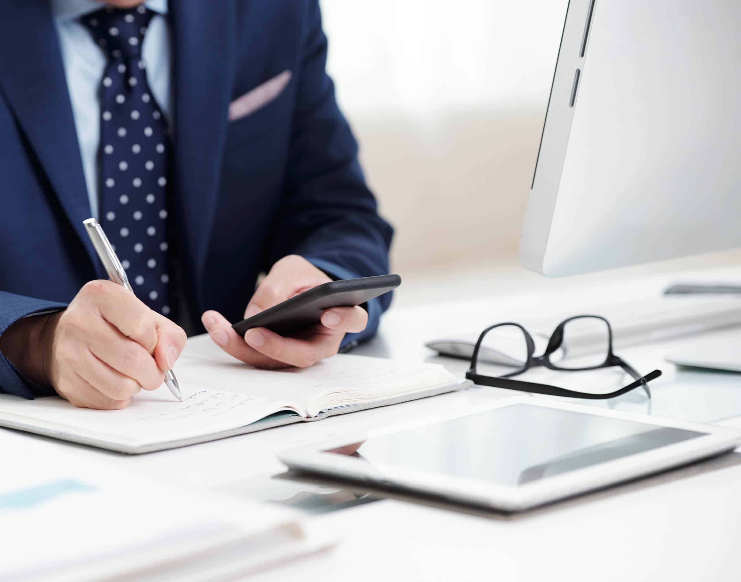 Cropped image of businessman checking messages in smartphone and taking notes in planner