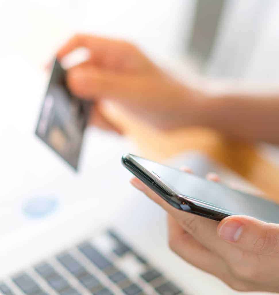 Hands holding a credit card using laptop computer and mobile phone for online shopping .